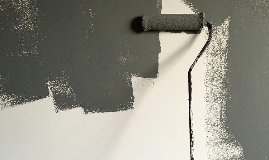 A paint roller applying a coat of grey protective coating across a white interior wall