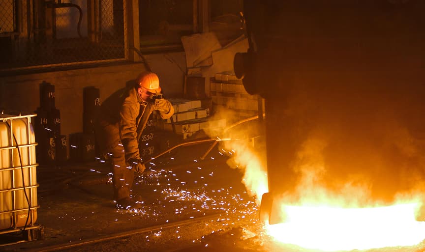 A steel worker tapping molten metal from a furnace in a steel mill, sparks flying from the stream