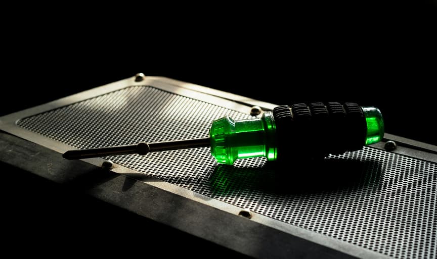 A screwdriver with a moulded soft-touch thermoplastic elastomer grip lying on a perforated steel plate